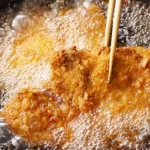 Friendo tonkatsu (milanesa o chuleta de cerdo empanada), comida frita japonesa