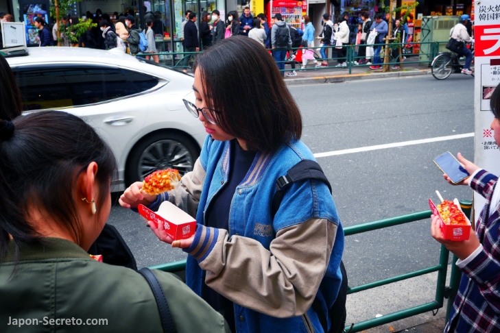 Chicas comiendo comida callejera en Okubo dori, calle principal 
