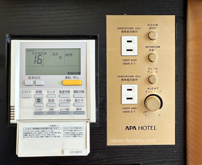 Mando a distancia del aire acondicionado y climatizador junto a enchufes en el cabecero de la cama de habitación de hotel Apa en Tokio