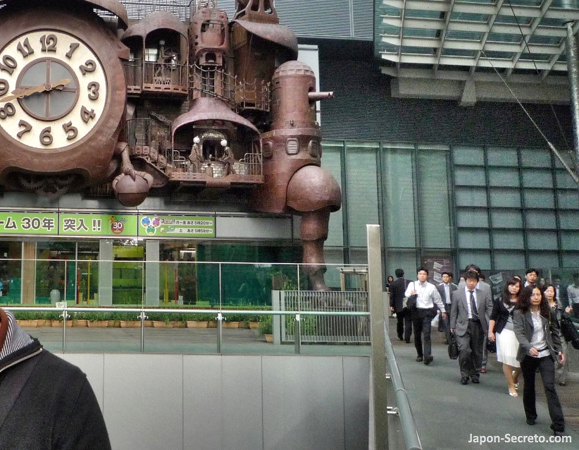 Asalariados (salary man) yendo al trabajao y pasando al lado del Reloj gigante Nippon TV Odokei o Nittere Odokei (日テレ大時計), diseñado por Hayao Miyazaki y situado en Shiodome Shiosite, en el barrio de Shinbashi en Tokio (distrito Minato)