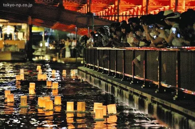 Gente participando con sus farolillos en el festival Asakusa Tōrō Nagashi (浅草とうろう流し) de farolillos flotando en el río Sumida